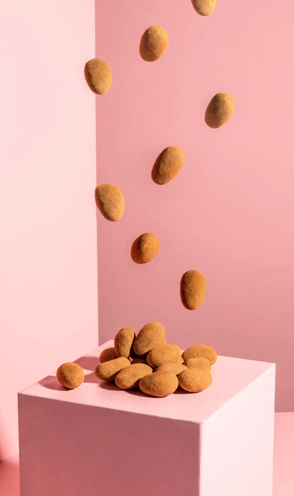 Almonds falling on pink block